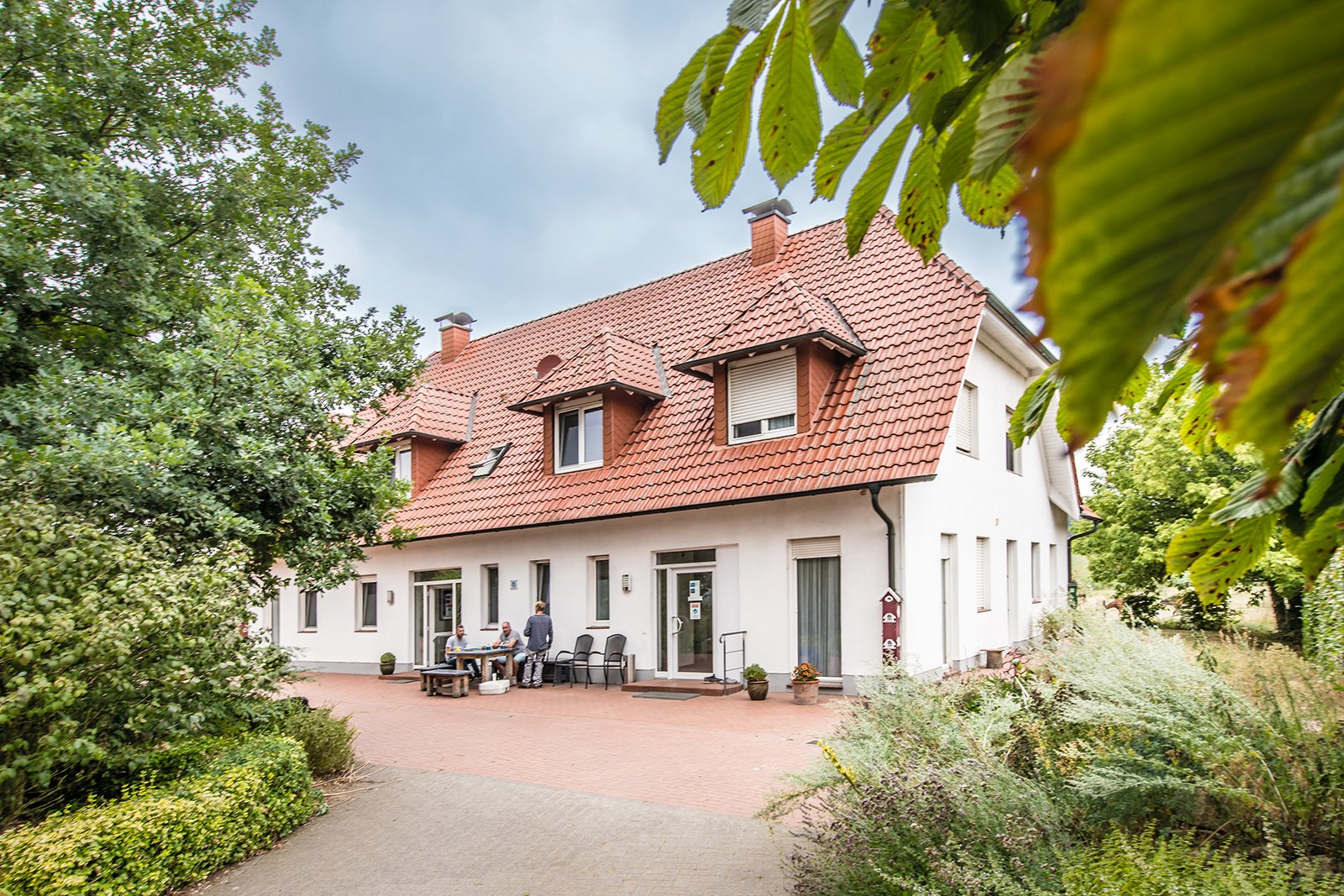 Wohnhaus im Grünen mit Bewohnern auf der Bank davor.