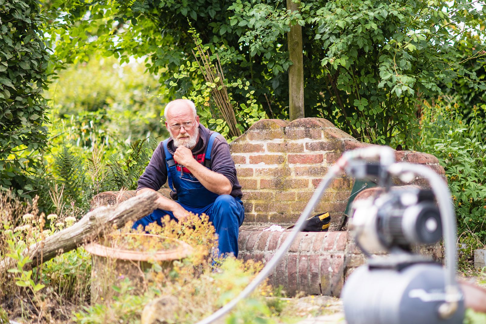 Ein Mann sitzt nachdenklich auf einer Steinbank im Garten